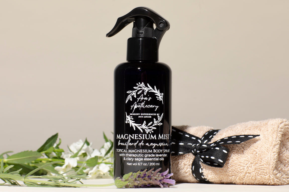 Black spray bottle labeled 'Magnesium Mist' with a towel and greenery on a light background
