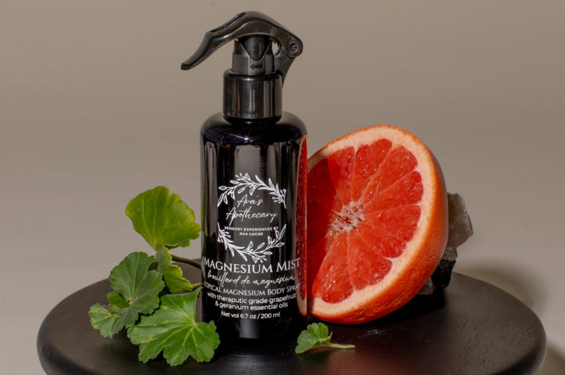 Black spray bottle with a label, half a grapefruit, and green leaves on a dark surface.