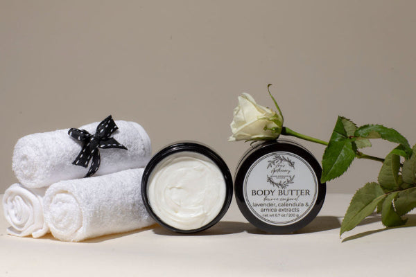 Two jars of body butter with rolled towels and a rose on a neutral background