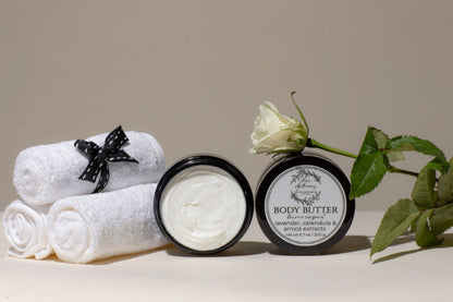 Two jars of body butter with rolled towels and a rose on a neutral background